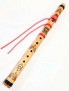 a wooden flute with red strings and designs on the top is laying on a white surface