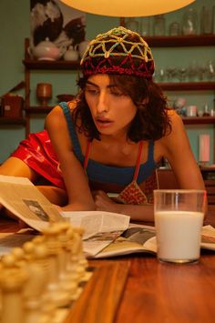 a woman sitting at a table reading a book with a glass of milk in front of her