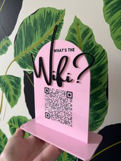 a hand holding up a pink card with qr code on it and palm leaves behind it