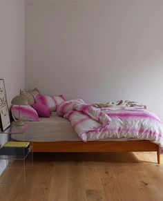 a bed sitting on top of a hard wood floor next to a window with pink and white pillows