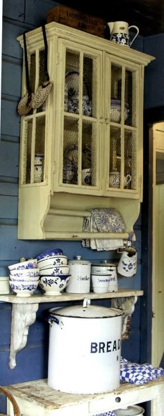 an old fashioned kitchen with blue walls and white dishes on the shelf, next to a wooden ladder