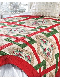 a bed with a red and green quilt on it's cover next to pillows