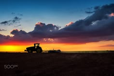 a tractor plowing a field at sunset