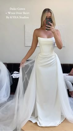 a woman taking a selfie wearing a white wedding dress and holding a cell phone