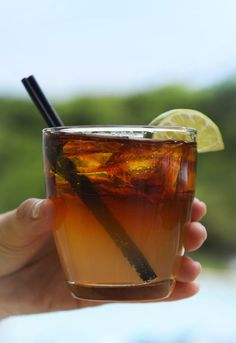 a hand holding a drink with a lemon wedge