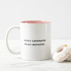 a pink and white coffee mug sitting next to a half eaten doughnut