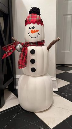 a large snowman with a red hat and scarf on it's head stands in front of a black and white checkered wall