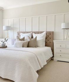 a bedroom with white bedding and pillows on the headboard, dressers and lamps