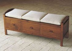 a wooden bench with three drawers and cushioned seat cushions on the bottom, sitting on a brick floor