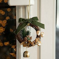 a christmas wreath hanging on the front door with bells and pine cones attached to it