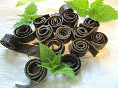 several rolled up chocolates with green leaves on the top and bottom, sitting on a white table cloth