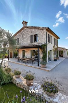 the house is surrounded by flowers and greenery, with an outdoor dining area in front