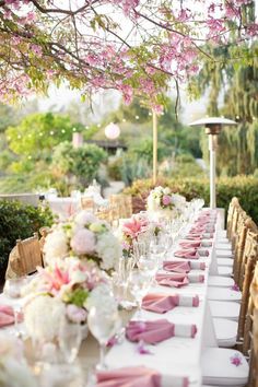 a long table with pink napkins and white flowers is set up for an outdoor dinner