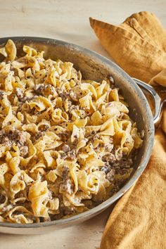 a skillet filled with pasta and meat on top of a wooden table next to a napkin