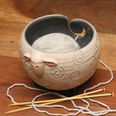 a bowl that has yarn in it and two knitting needles next to it on a wooden surface