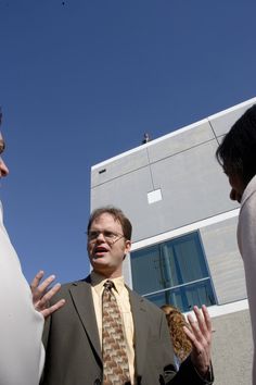 two men are talking to each other in front of a building with a sky background