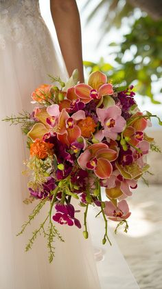 a bride holding a bouquet of pink and orange flowers on her wedding day at the beach