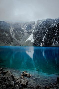 the mountain is covered in snow and blue water, with rocks on the ground below