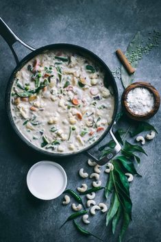 a pan filled with food next to some leaves and spoons on top of a table