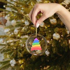 a hand holding a glass ornament with a rainbow triangle on it and a pine tree in the background