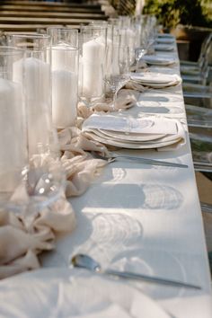 a long table is set with white plates and silverware, candles and napkins