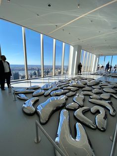 people are standing in the middle of a room with large windows and sculptures on the floor