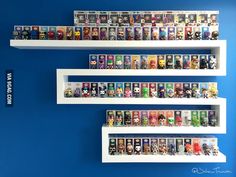 three white shelves filled with different types of action figures on top of each other in front of a blue wall