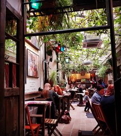 people sitting at tables in an alleyway with plants growing on the walls and ceiling