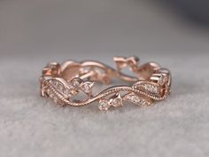 a rose gold wedding ring with diamonds on the sides and leaves in the middle, sitting on a white surface