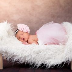 a baby girl in a pink dress sleeping on a wooden bed with fluffy white blankets