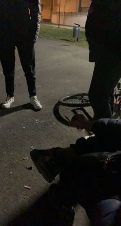 two men standing next to each other near a bike tire on the street at night