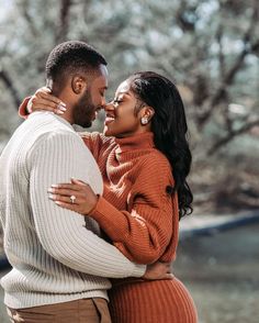 a man and woman embracing each other in front of trees