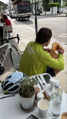 a person sitting at a table with food and drinks in front of them on the sidewalk