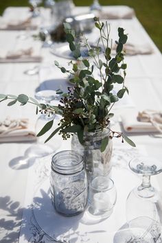 the table is set with mason jars and greenery