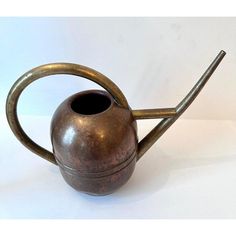 a metal watering can with a long handle on it's side, sitting on a white surface