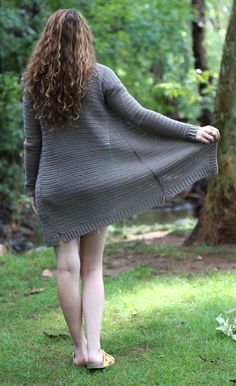 a woman is walking in the grass with her back to the camera, wearing a gray sweater