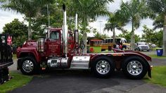 a red semi truck parked on the side of a road next to palm trees and other vehicles