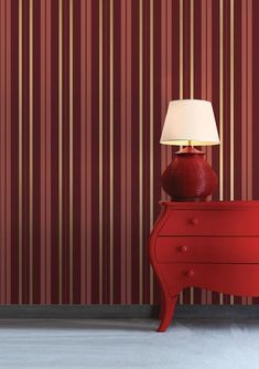 a red dresser with a lamp on it in front of a striped wallpapered room