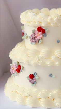 a three tiered cake with white frosting and colorful flowers on the top layer