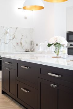 a kitchen with marble counter tops and black cabinets, white flowers on the island top