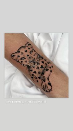 a cheetah tattoo on the arm with black dots and heart shapes around it