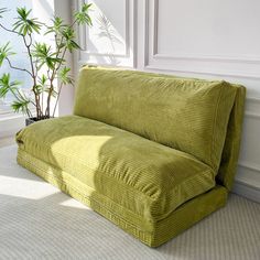 a green couch sitting next to a potted plant on top of a white floor