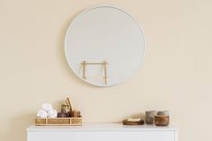 a white dresser with a round mirror on the wall above it and candles in front of it