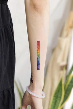 a person with a small rainbow tattoo on their left arm, holding onto a plastic tube