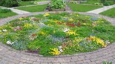 a circular garden with many different flowers in the center, surrounded by brick walkways