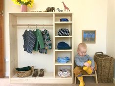 a baby sitting on a chair in front of a shelf with clothes and shoes hanging from it