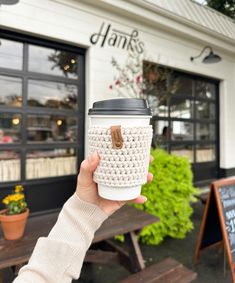 a person holding up a coffee cup in front of a building