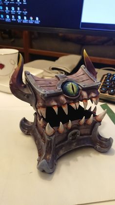 a computer monitor sitting on top of a desk next to a toy dragon head with sharp teeth