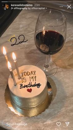 a birthday cake sitting on top of a table next to a glass of wine