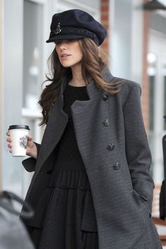 a woman is holding a coffee cup and wearing a black hat while walking down the street